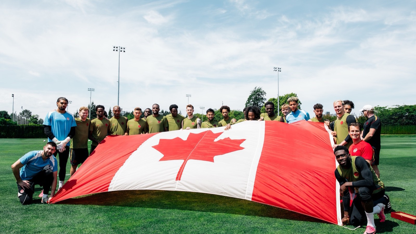 Los jugadores de la selección masculina de Canadá posan con una gran bandera nacional en su entrenamiento
